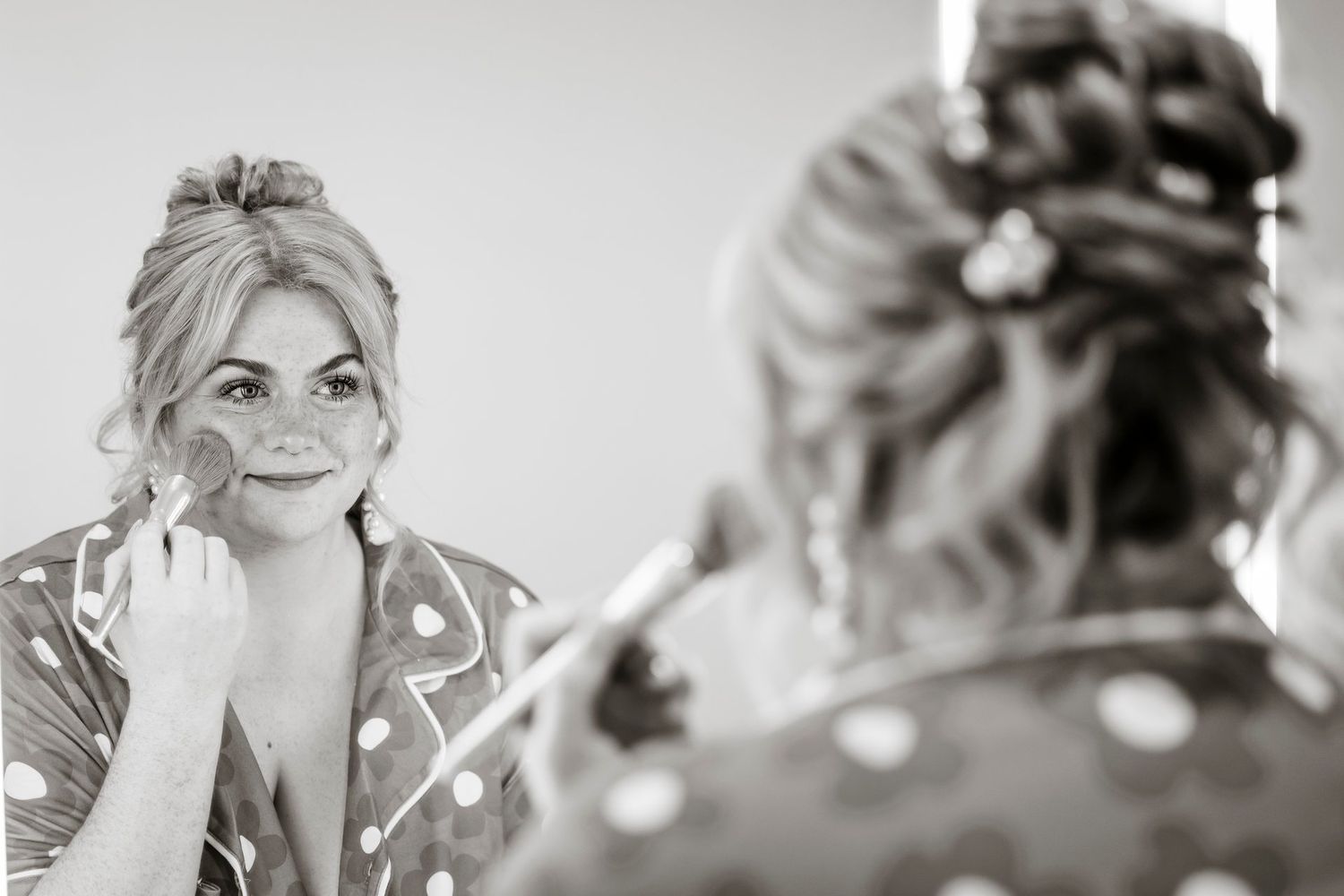 A black and white reflection shot of someone looking in a mirror during wedding preparations.