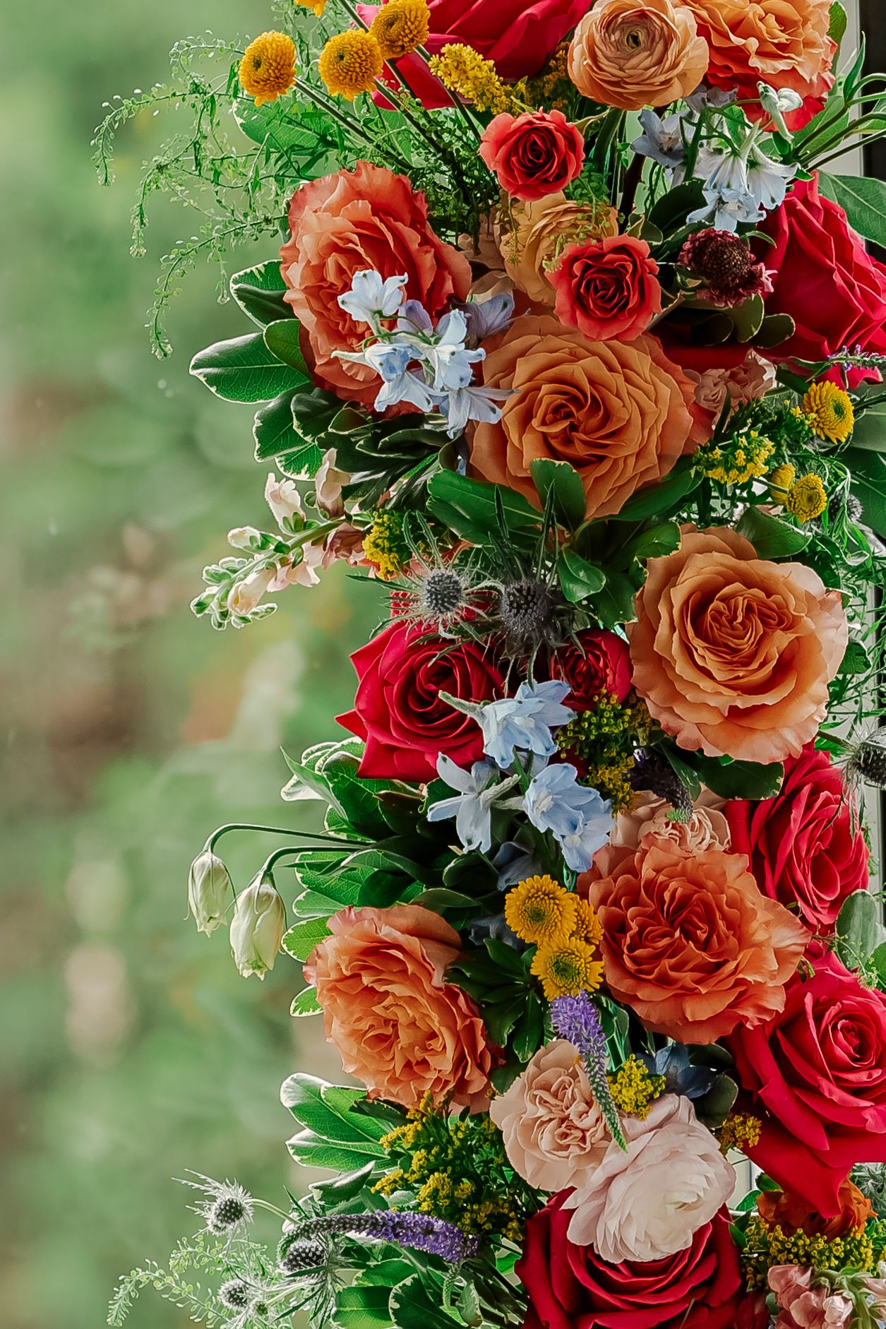 Vibrant floral arrangement featuring red and peach roses with delicate white flowers and yellow accents against a blurred green background.