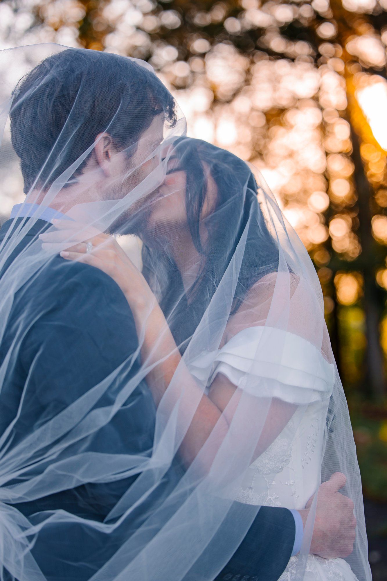 A romantic wedding couple shares tender moments under flowing fabric at sunset.