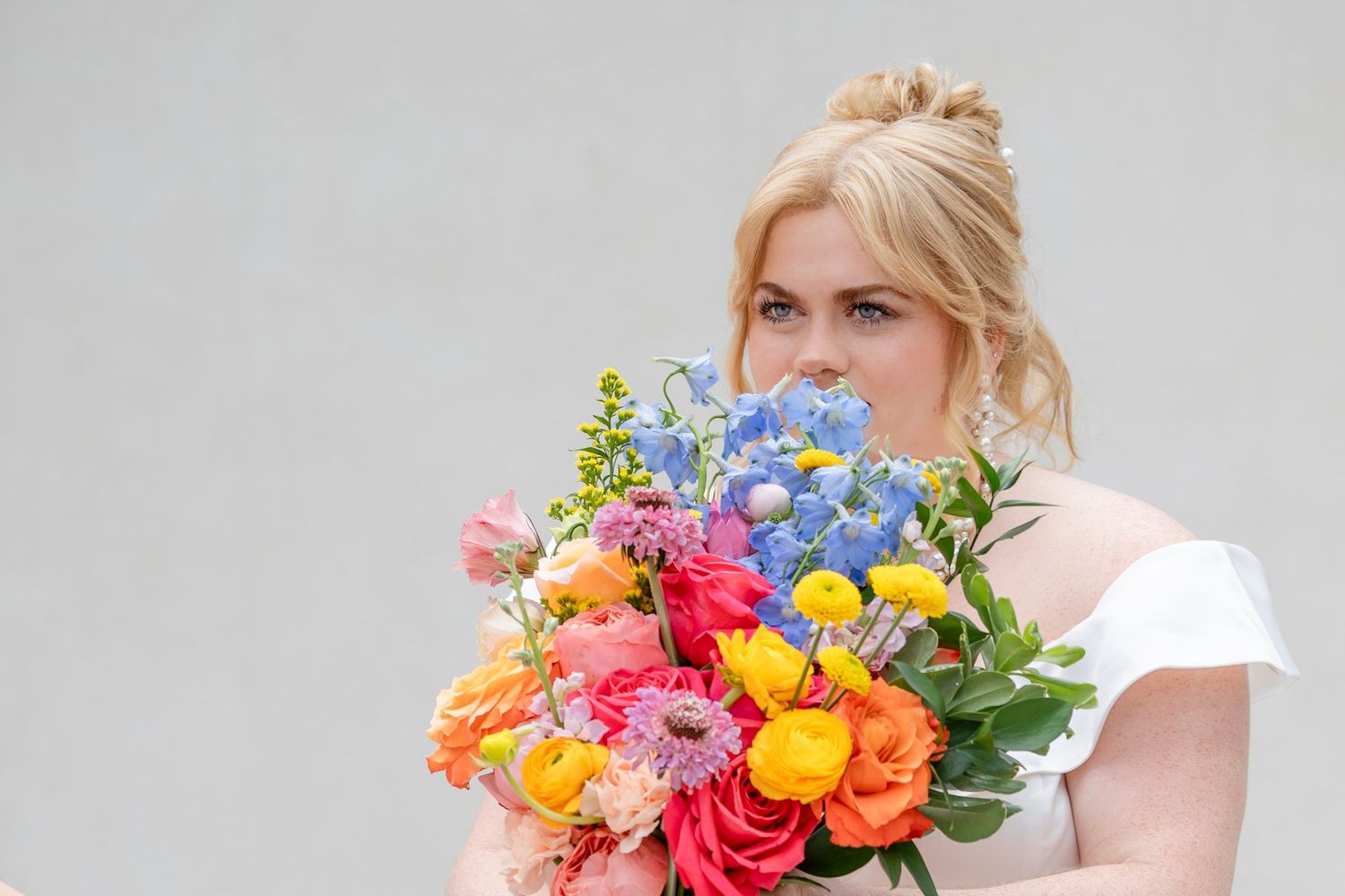 A vibrant bouquet of colorful spring flowers including roses, delphiniums and tulips against a light gray background.