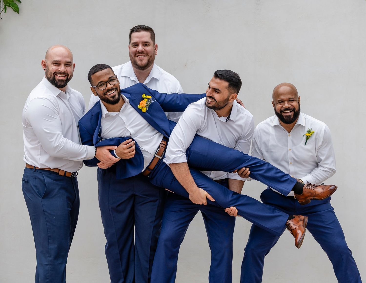 Groomsmen in navy blue pants and white shirts striking fun poses in a group photo lineup.