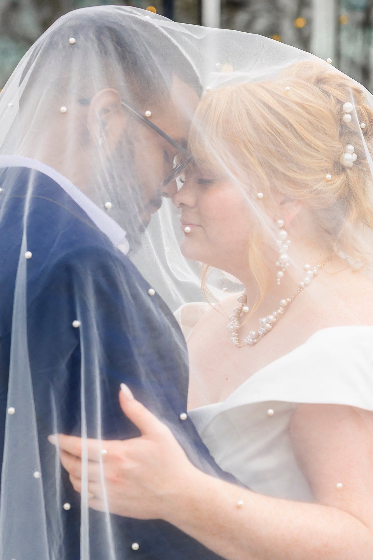 Intimate moment between newlyweds under a pearl-studded veil.