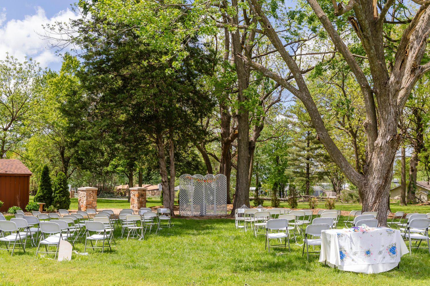 Garden wedding venue setup with white chairs and tables arranged under mature trees.