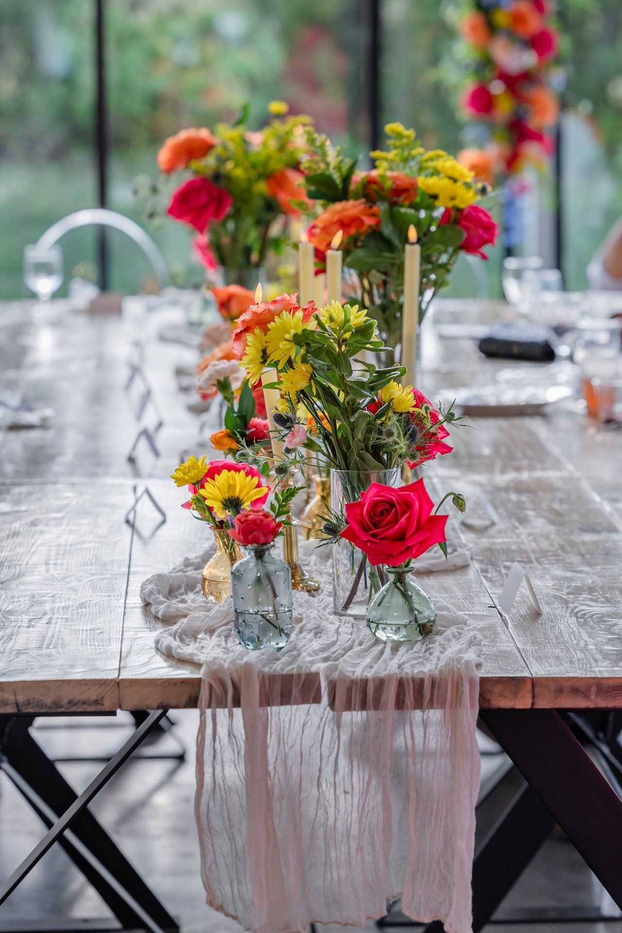 Colorful floral centerpieces with roses and wildflowers displayed on a rustic wooden table with flowing white table runner.