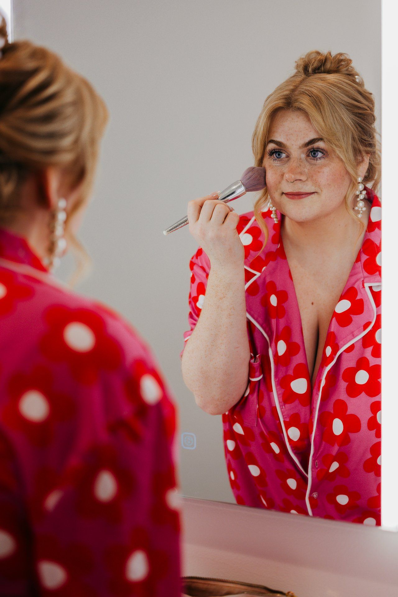 Woman in red polka dot dress applying makeup while looking in mirror.