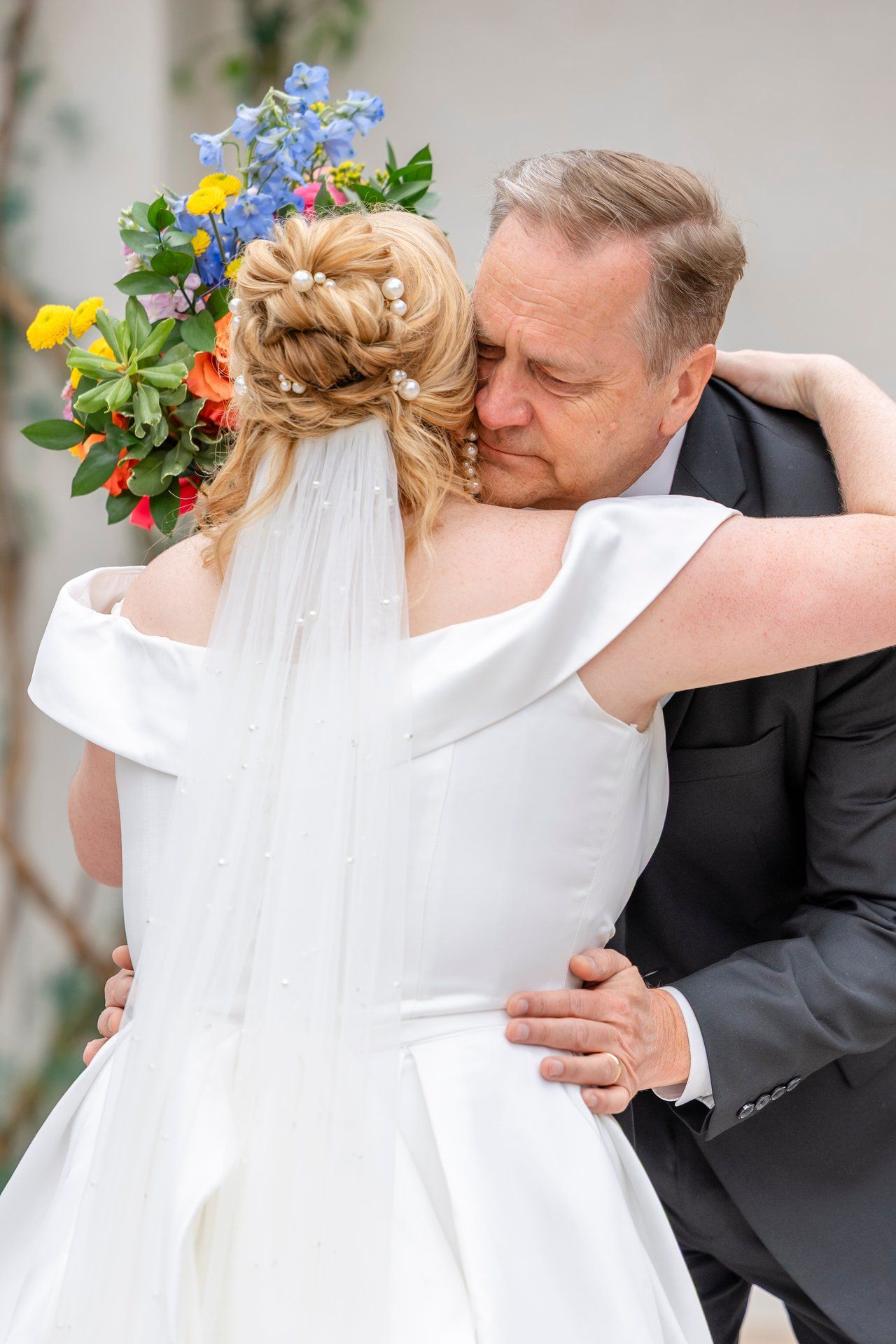 A tender moment between a bride in a white dress with flowers and a person in a black suit during a wedding embrace.