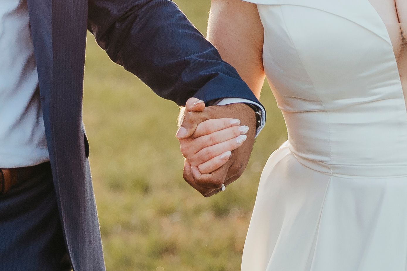 Close-up of newlyweds holding hands showing wedding attire details.