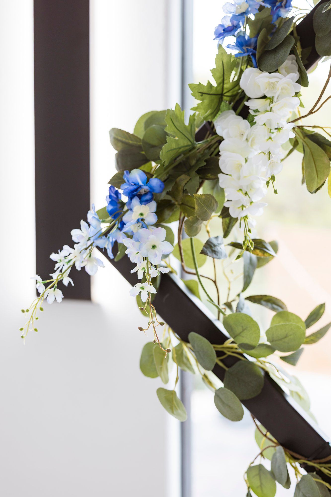 White and blue artificial flowers with green foliage intertwined between white fence railings.