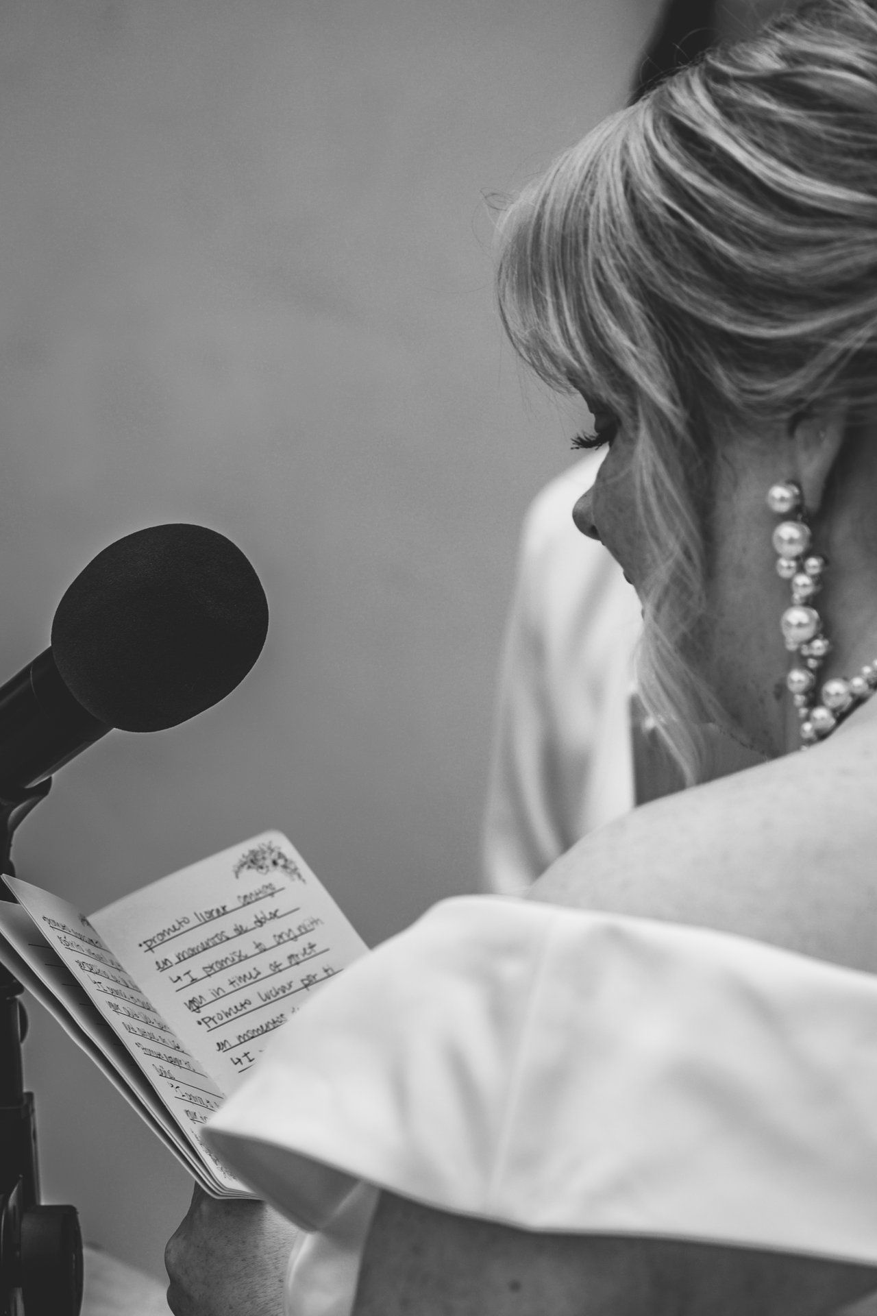 A person in a white jacket reads sheet music while standing at a microphone for a performance.