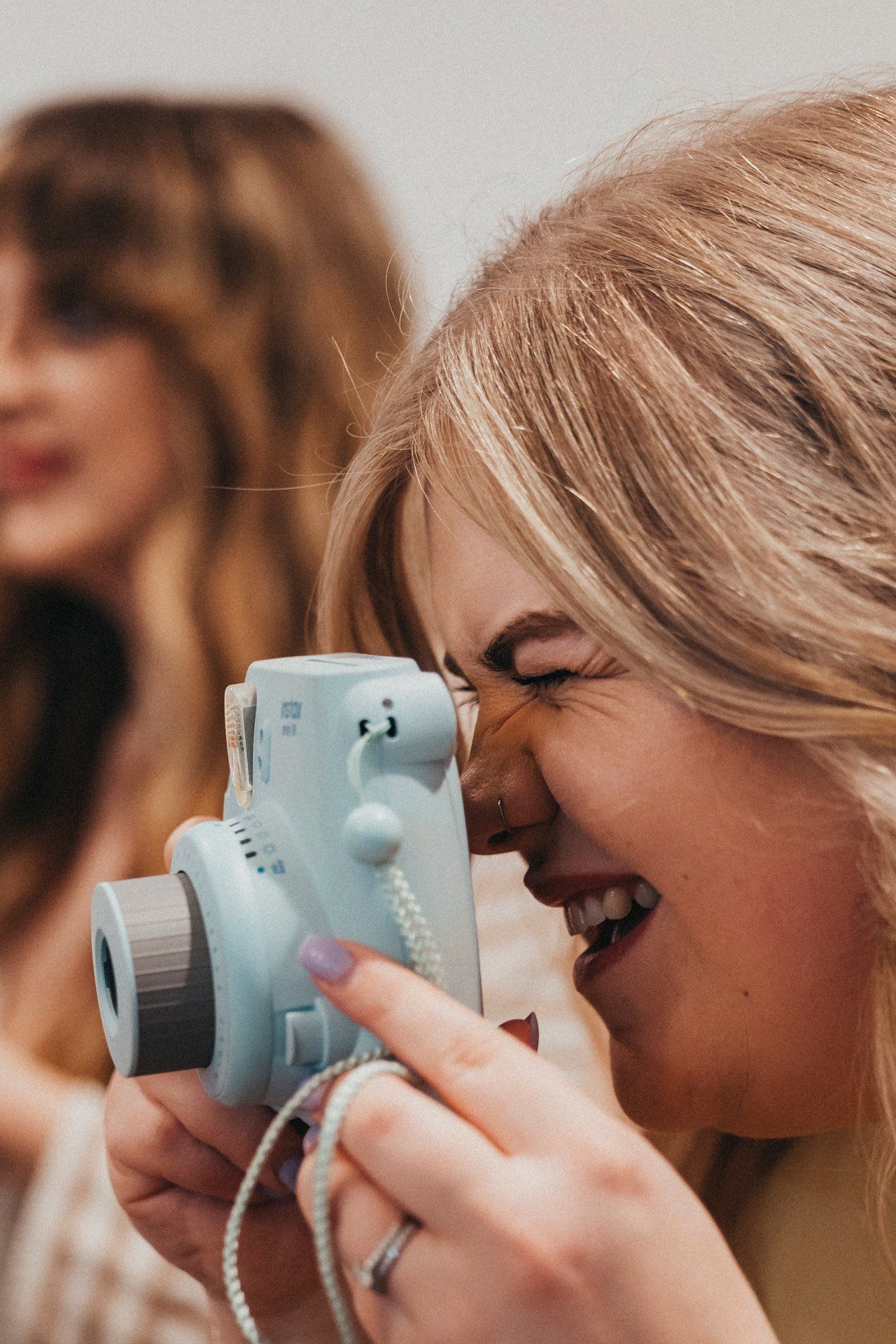 A photographer uses a light blue instant camera with a joyful expression.