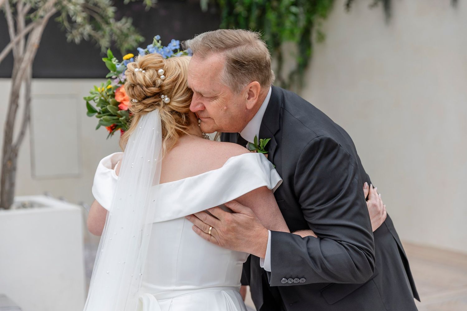 A tender moment captured at a wedding as two people share a loving embrace in an outdoor garden setting.