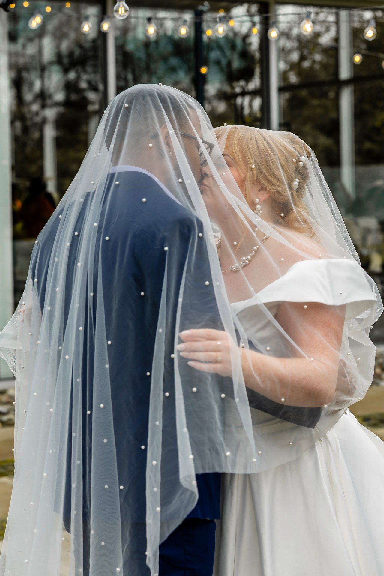 A couple shares an intimate moment under an elegant pearl-studded wedding veil on their special day.