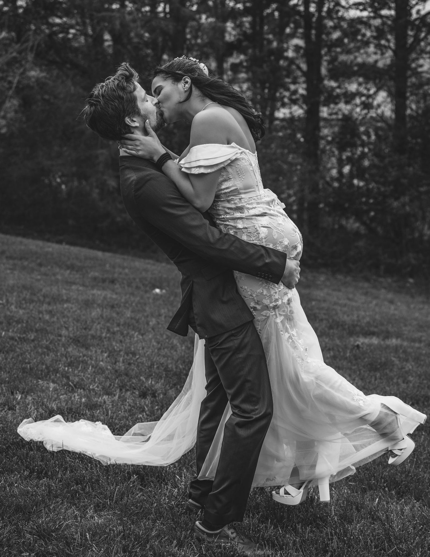 A romantic black and white wedding photo captures a couple embracing on a grassy hillside with the gown flowing in the breeze.