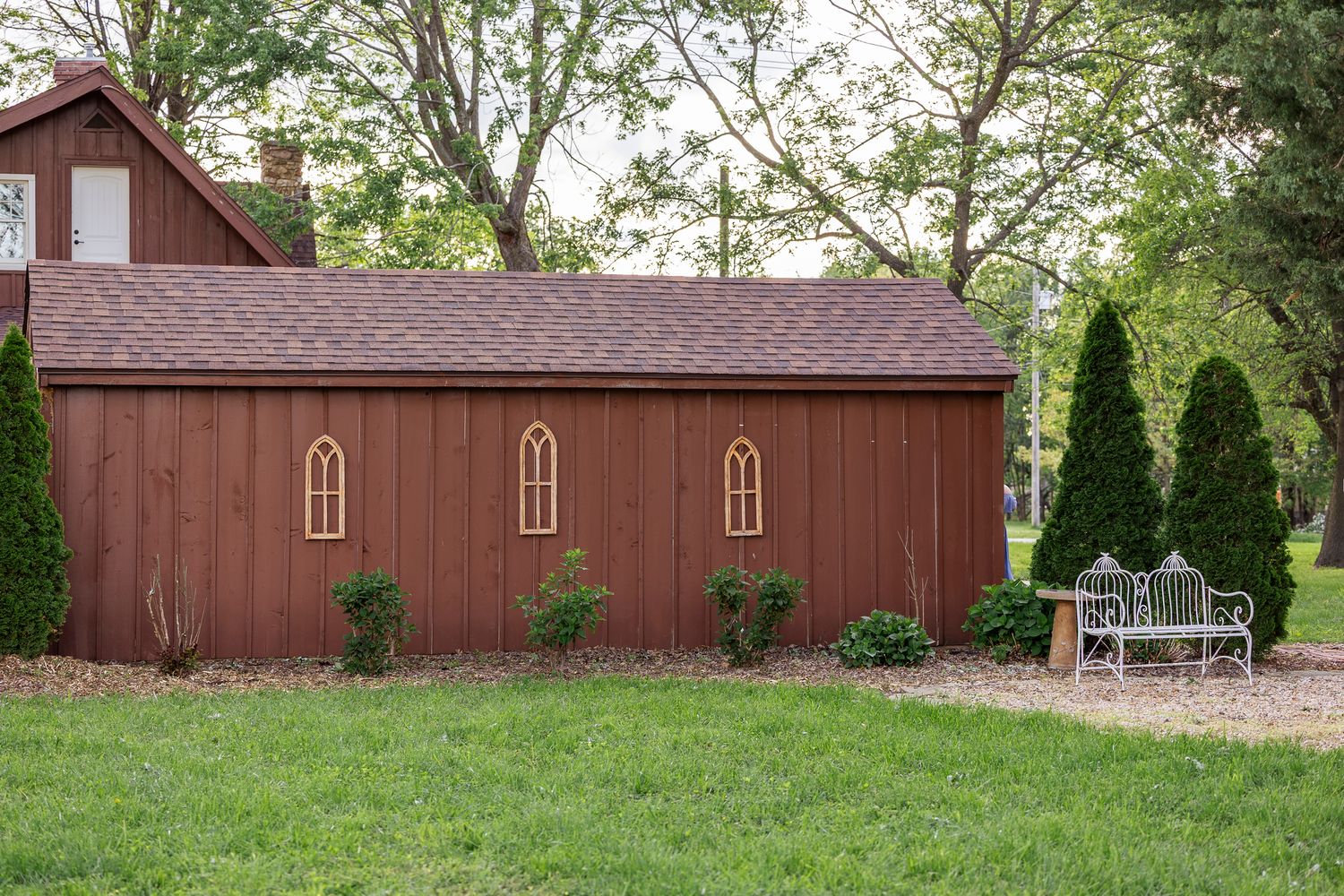 A long wooden red barn with Gothic-style windows is viewed from different angles in a series of photos.