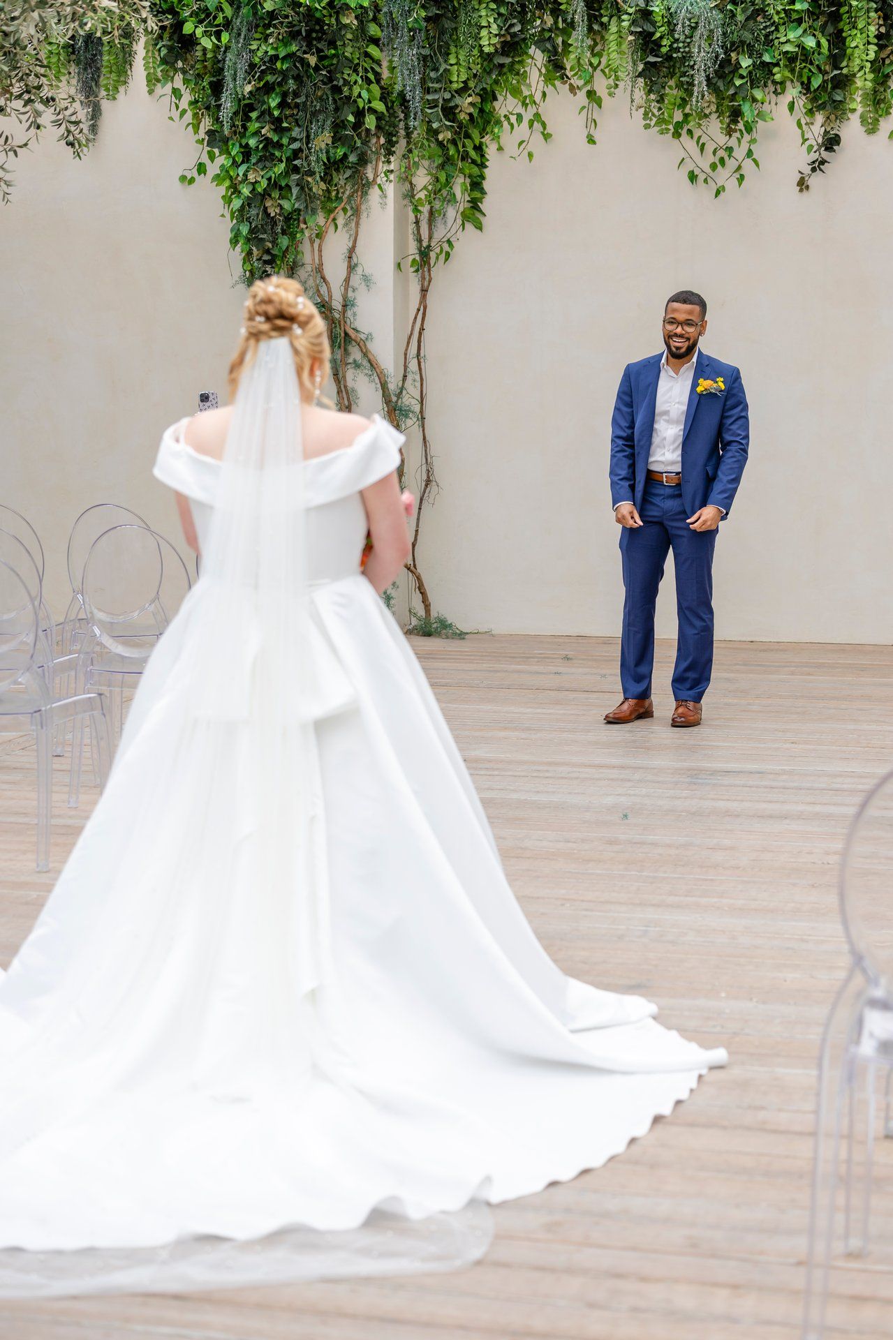 A first look wedding moment captured on a terrace with cascading vines and modern ghost chairs as decor.