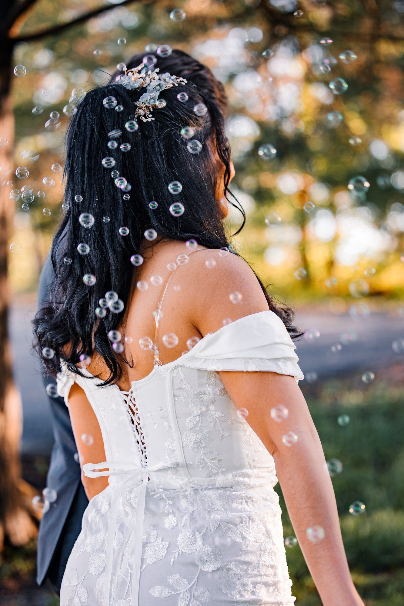 Back view of bride in lace dress with bubbles floating around her in dreamy outdoor wedding setting.