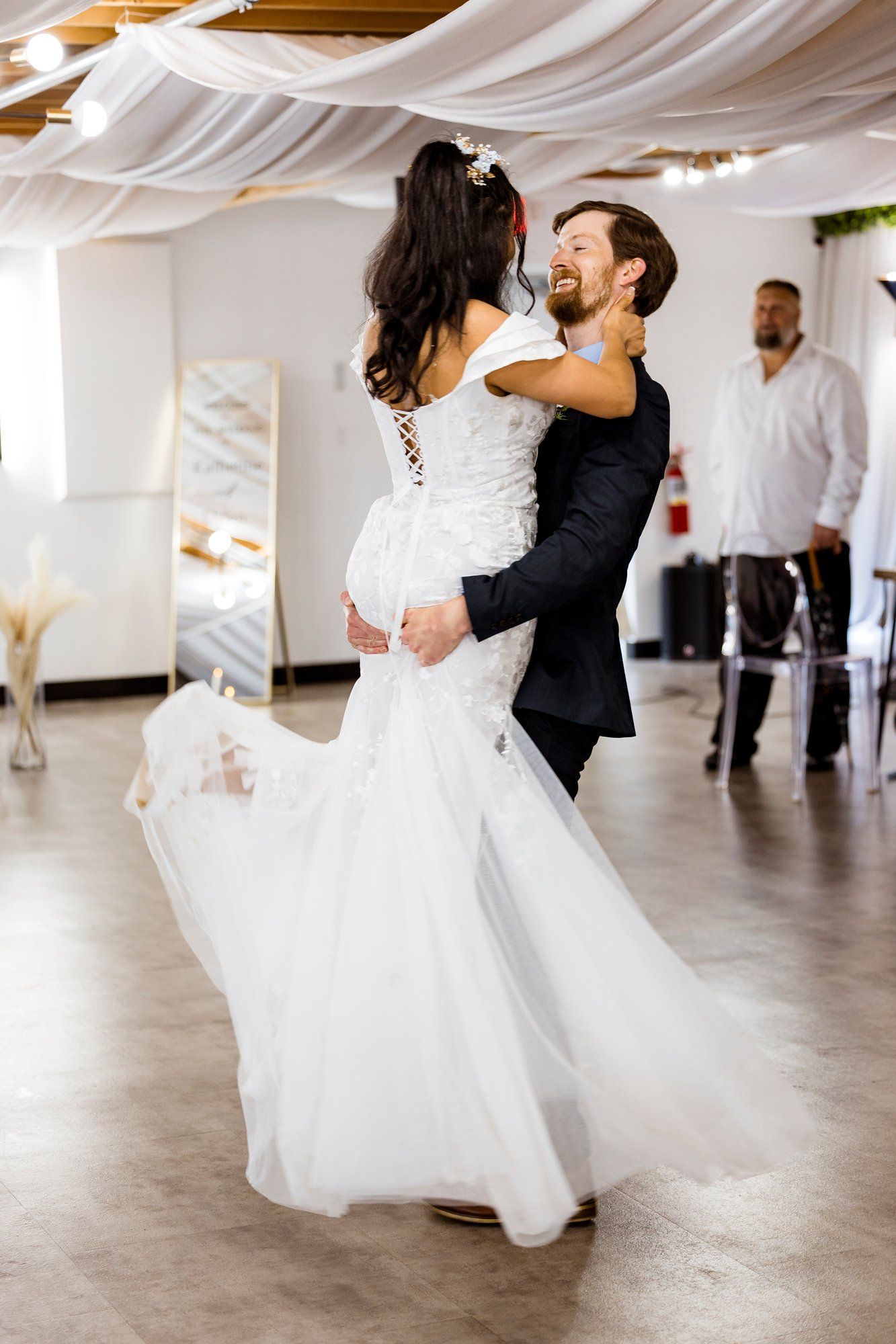 A couple shares their first dance at their wedding reception under flowing white fabric draped from the ceiling.
