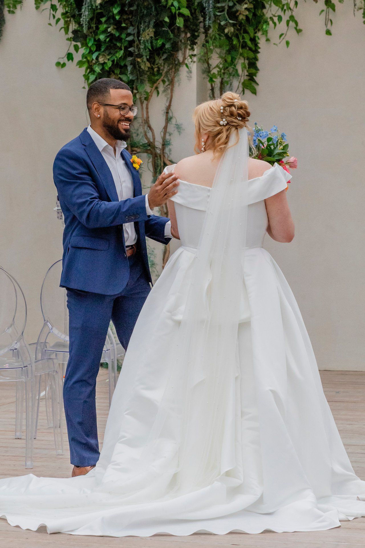 A couple sharing a joyful moment during their wedding, with the bride in a white gown and groom in a blue suit.