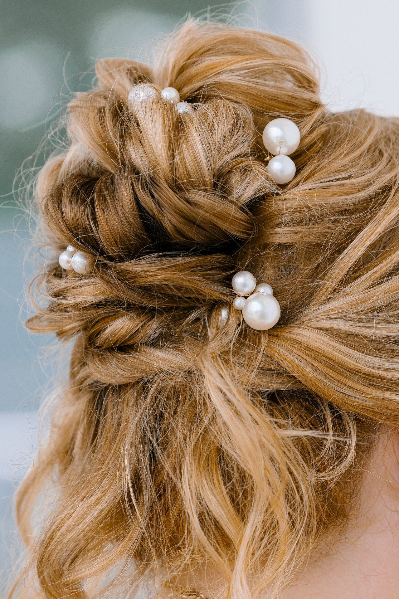 Close-up of an elegant updo hairstyle adorned with pearl-like hair pins in warm blonde tones.