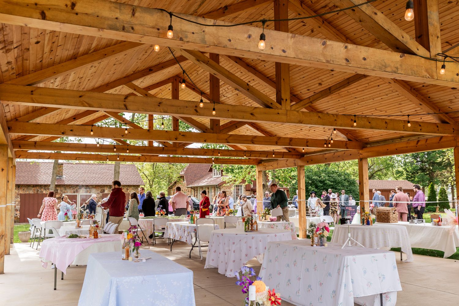 Reception tables set under rustic wooden beams in an outdoor pavilion decorated with pink floral centerpieces.