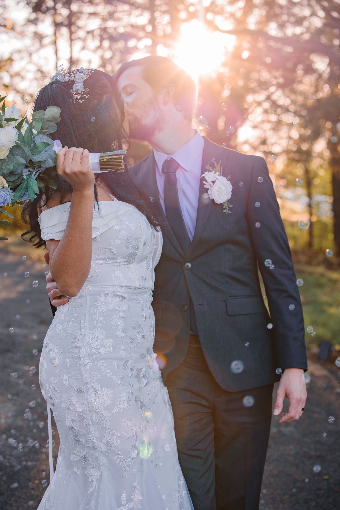 Newlyweds share intimate moments during a sunset photo session with bubbles floating through the air.