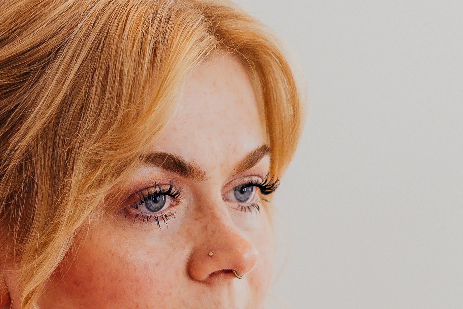 Close-up detail of eye makeup and strawberry blonde hair against a light background.