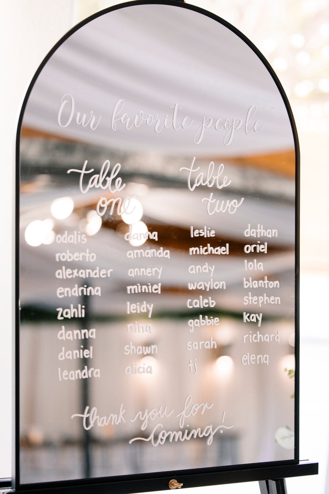 Arched mirror signs displaying wedding seating arrangements in white calligraphy lettering.