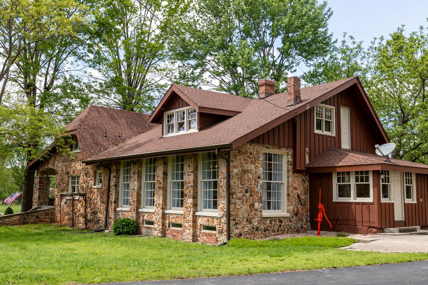 Rustic stone and wood cottage with red-brown roof features a sunroom with multiple windows and charming architectural details.