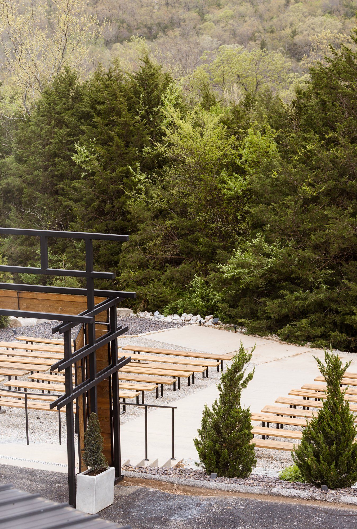 Wooden benches arranged in rows outdoors with evergreen trees and black railings creating an amphitheater-style seating area.
