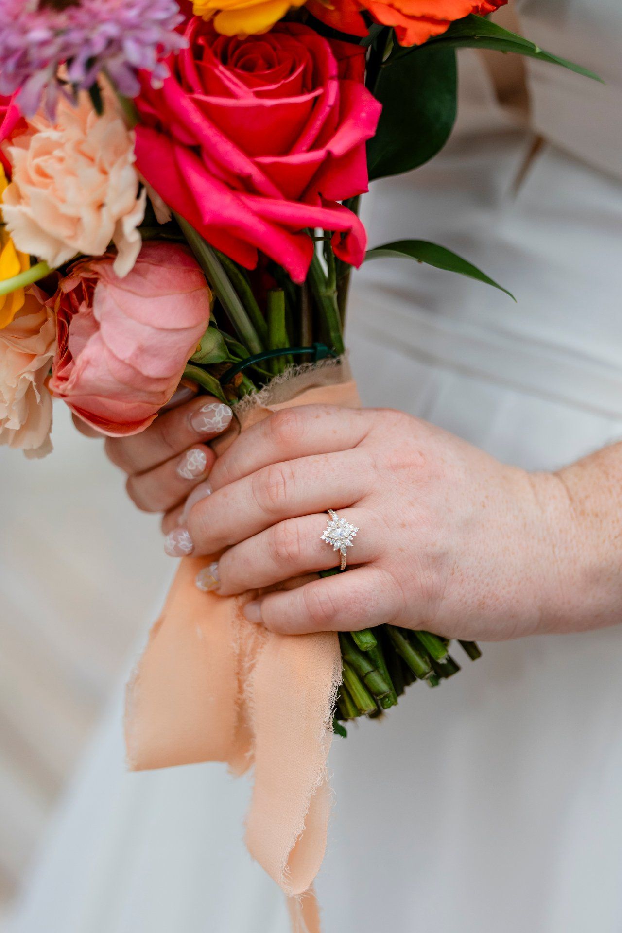 Close up of hands holding a vibrant bouquet of roses with a sparkling engagement ring on display.