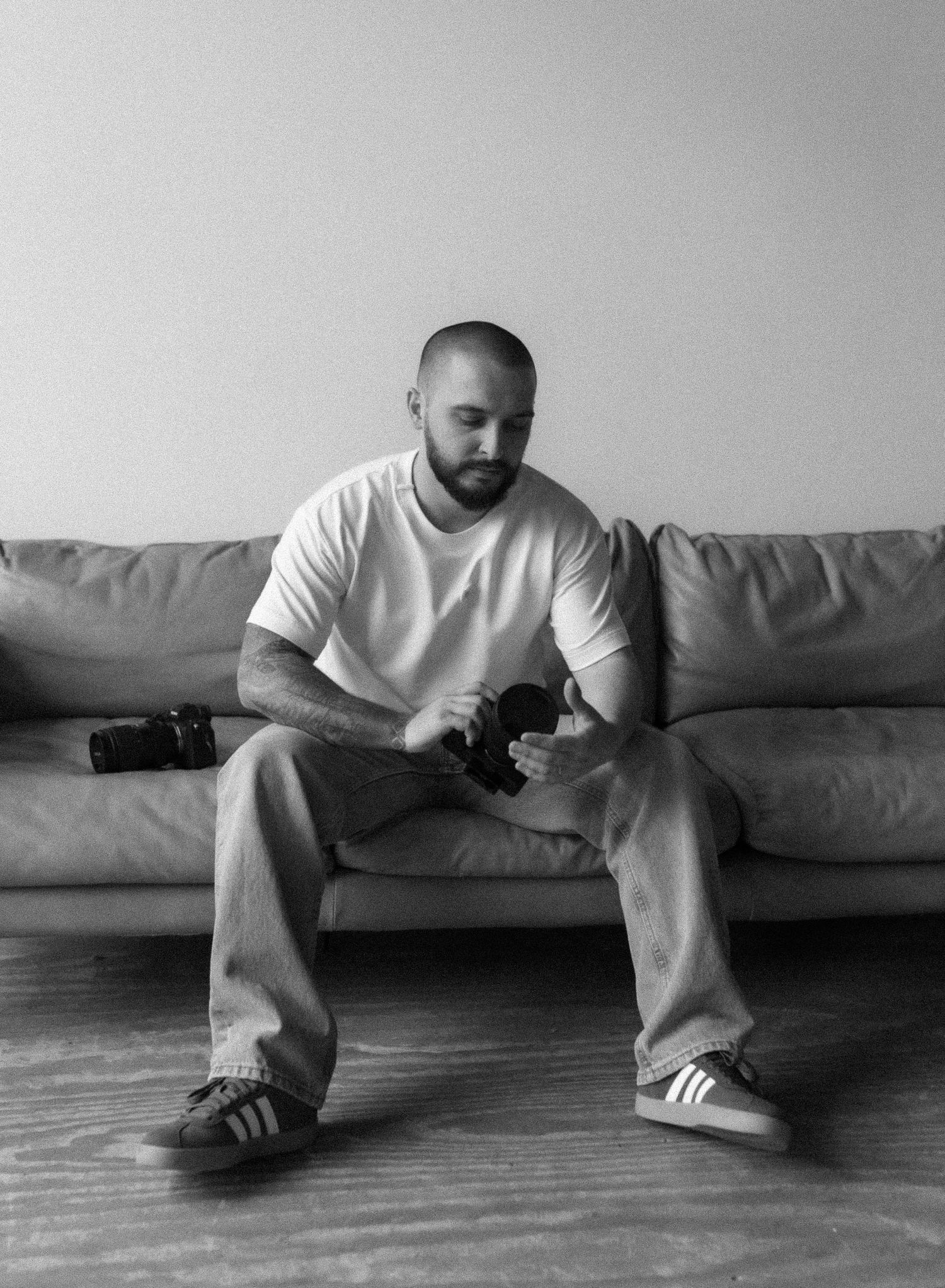 A black and white photograph shows someone sitting on a couch in a white shirt and jeans with sneakers.