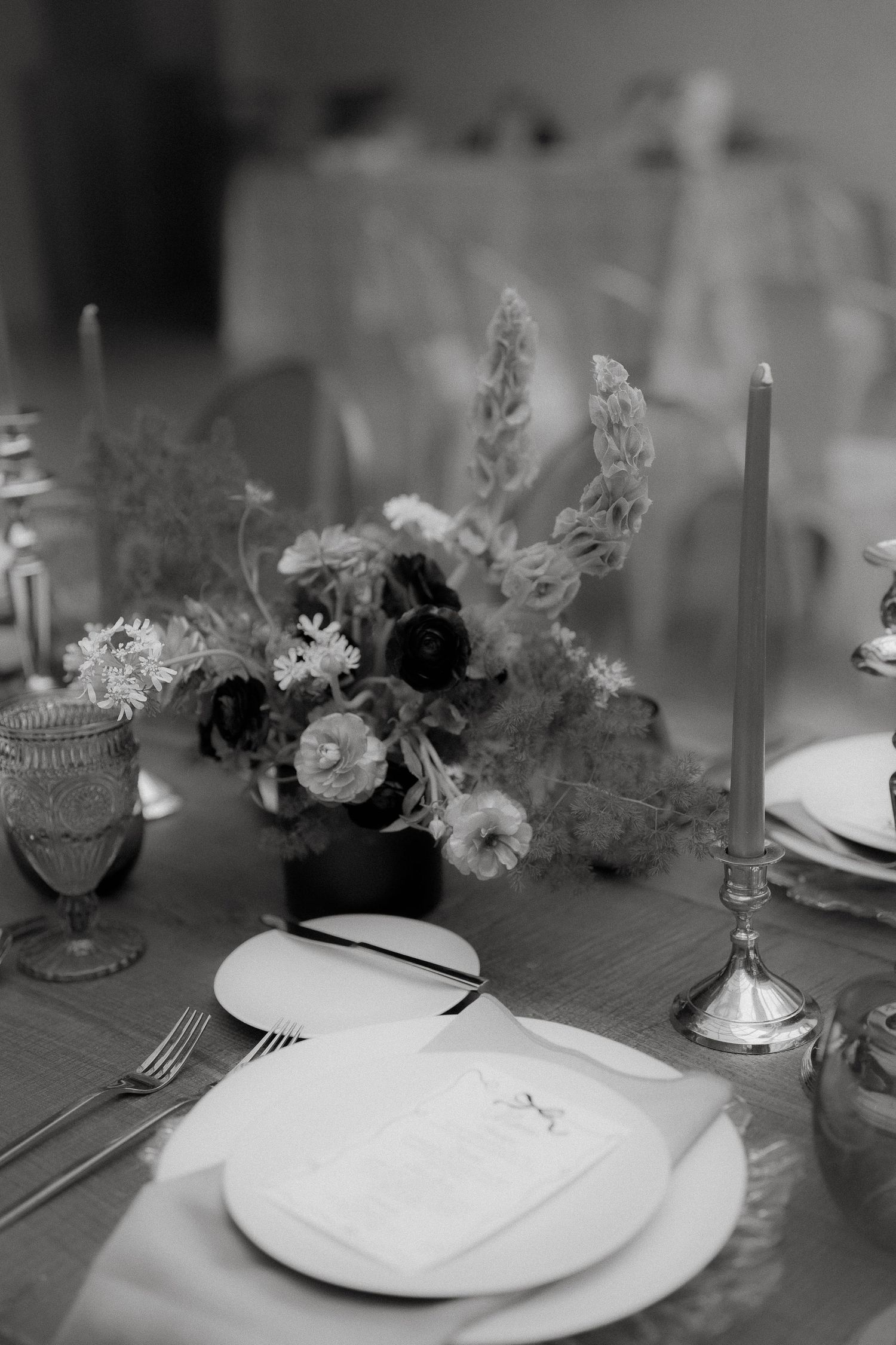 Black and white photograph of an elegant table setting with floral centerpiece, taper candle, and formal place settings.