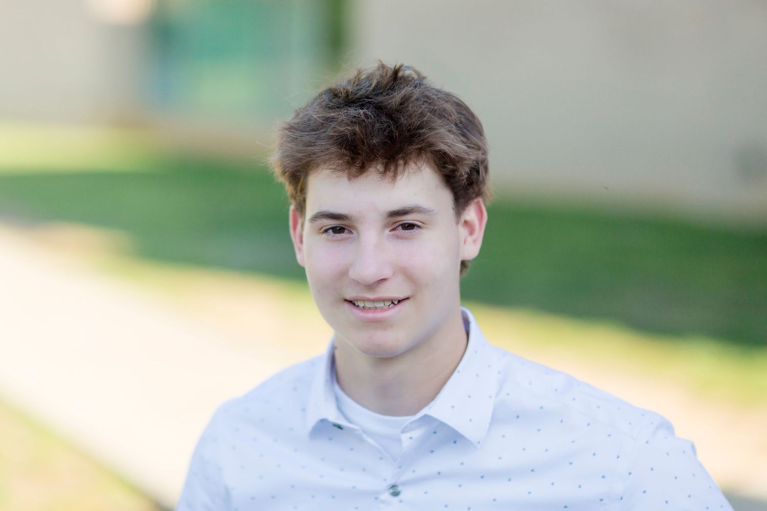 young man in white collared shirt smiling for senior photo; blurry background