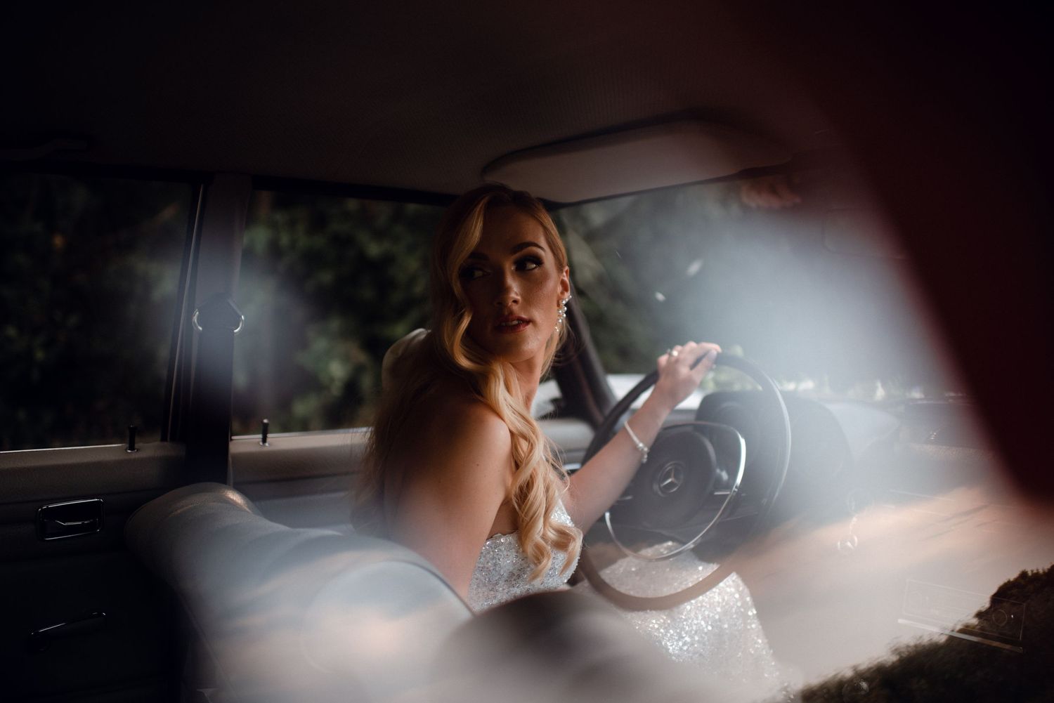 Elegant bridal portrait behind the wheel of a classic Mercedes with cinematic lighting