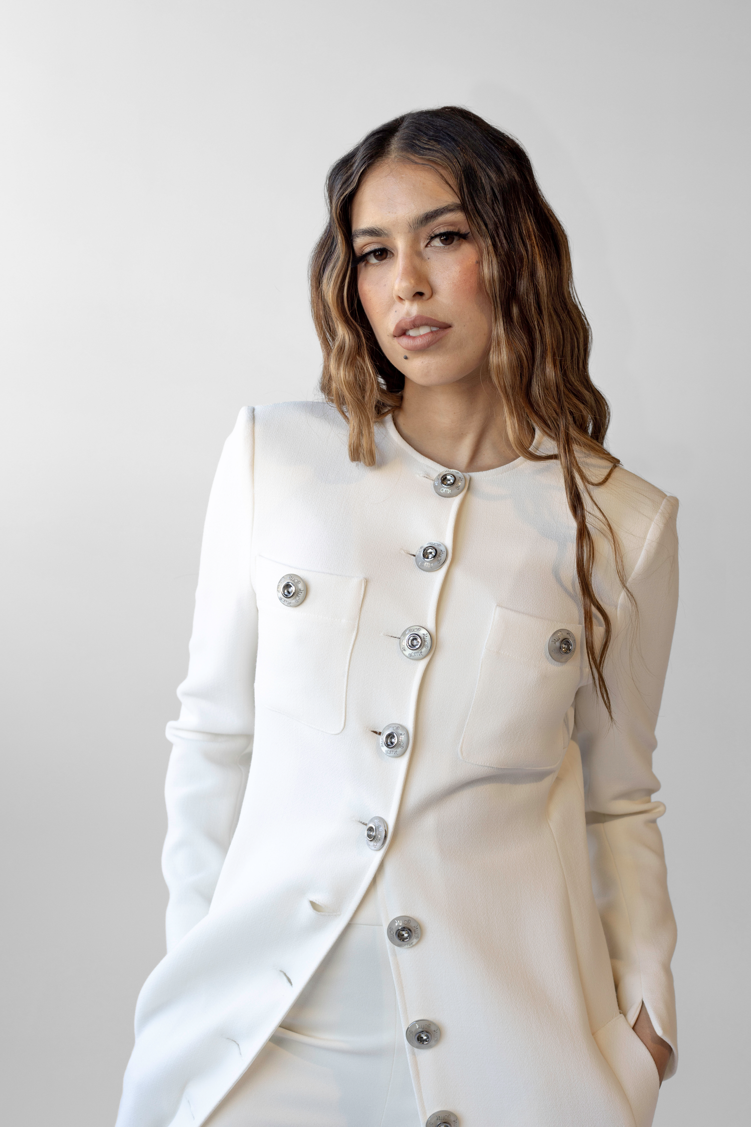 Stylish white button-down coat with silver accents worn against neutral gray studio backdrop.