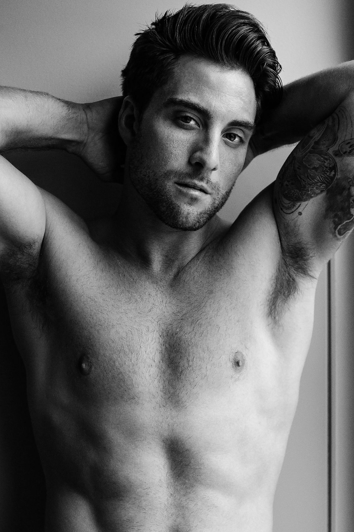 Black and white portrait of athletic man with tattoos in dramatic lighting.
