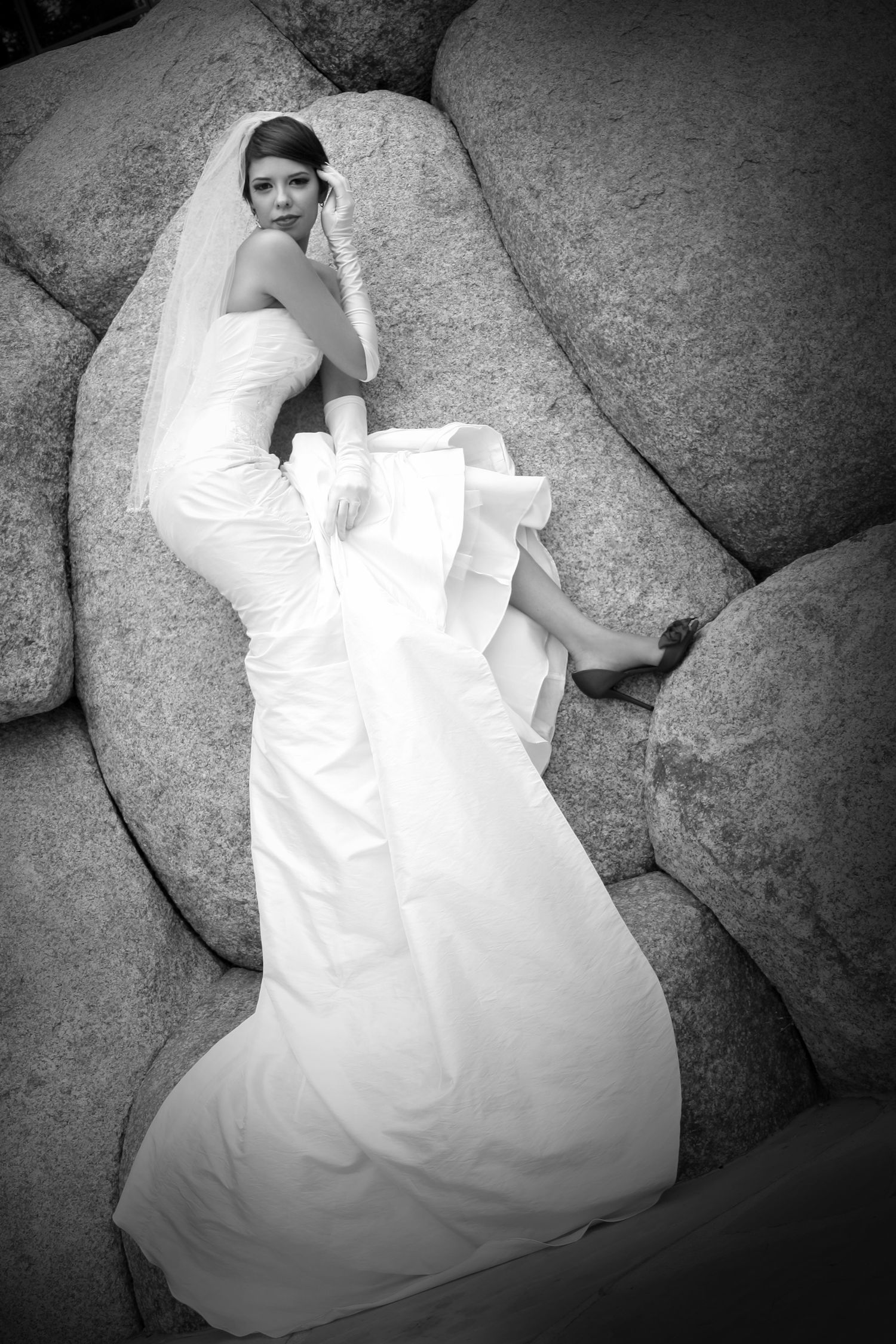 A black and white bridal portrait showing a wedding dress flowing over coastal rocks.