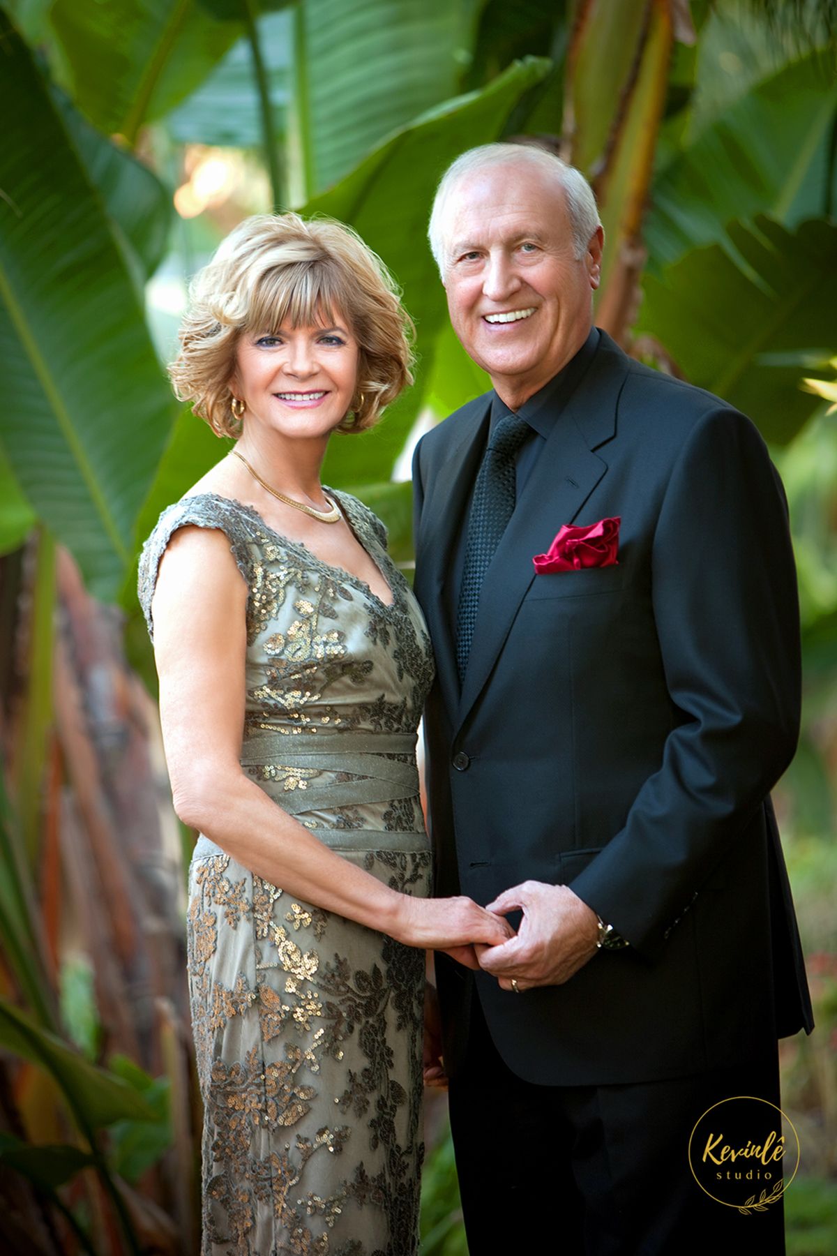 Elegant mature couple poses in formal attire against tropical garden backdrop.