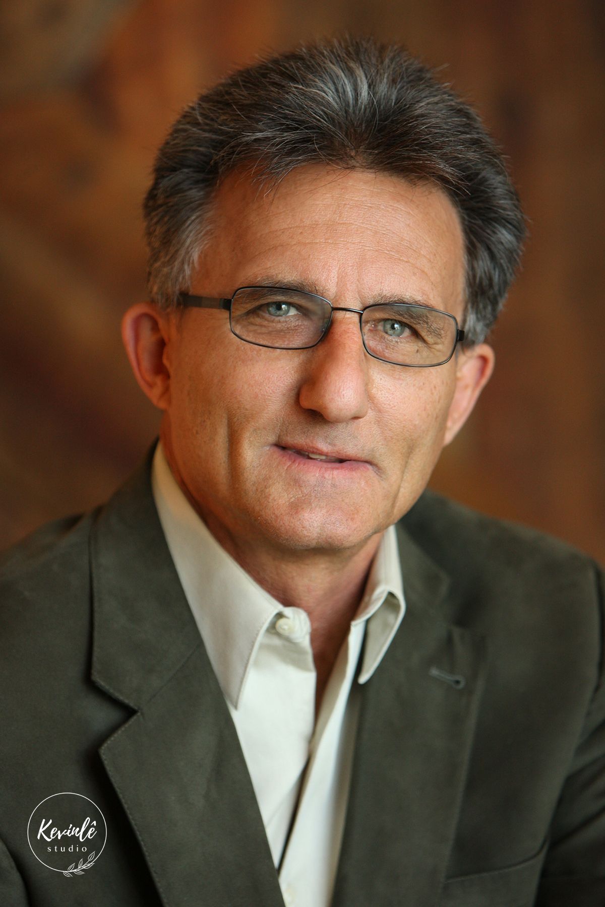 Professional headshot of a middle-aged man wearing glasses and a casual blazer.
