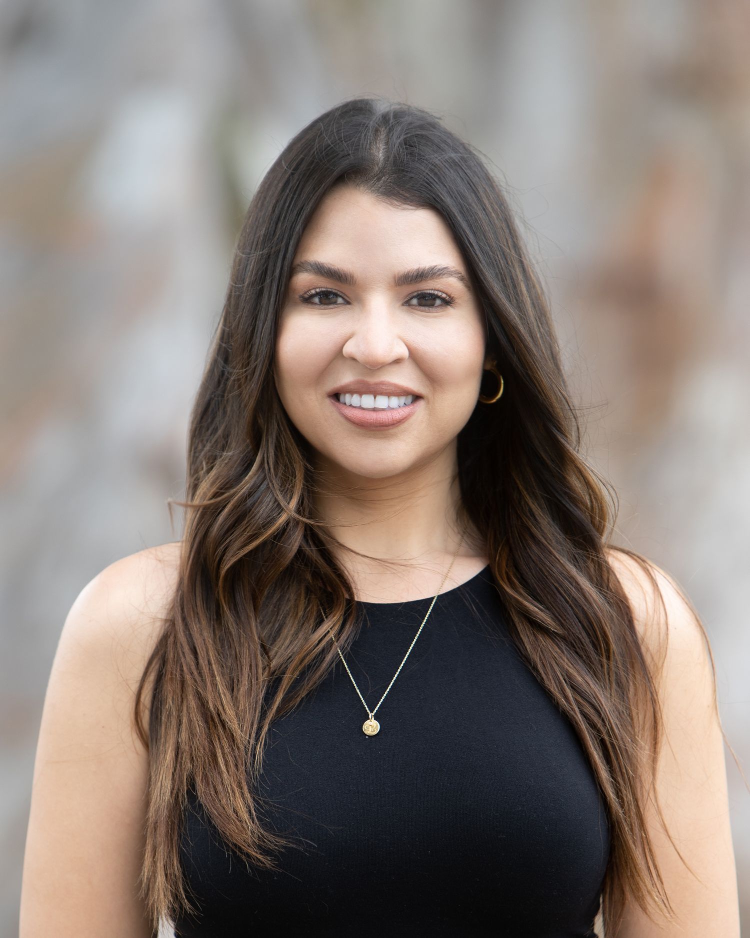 Professional headshot of a young woman with long brown hair wearing a black sleeveless top.