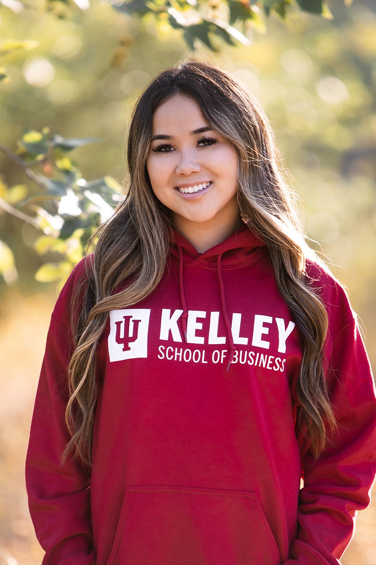 Student wearing a red Kelley School of Business hoodie smiles in sunny outdoor setting.