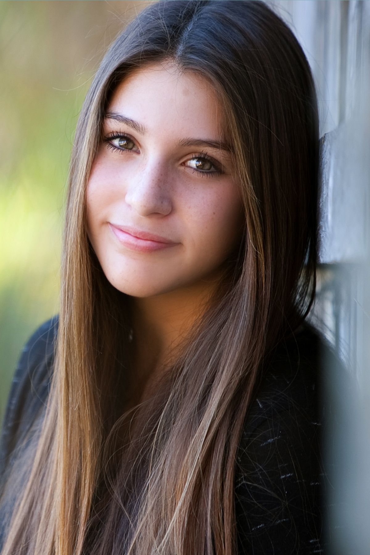 Portrait set showing a brunette teen in four similar expressions showing a soft smile against a blurred background.