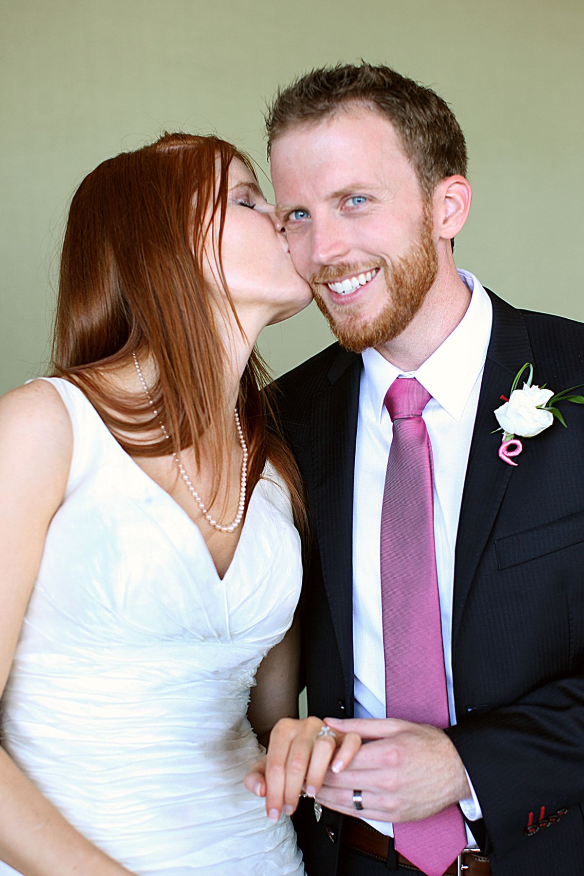 Couple sharing romantic moments in formal wedding attire with pink tie detail.