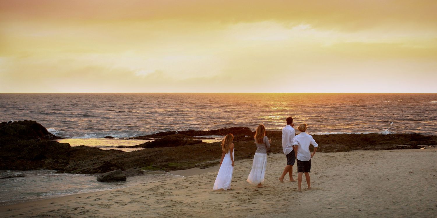 Three people walking on rocky beach during golden sunset by the ocean.