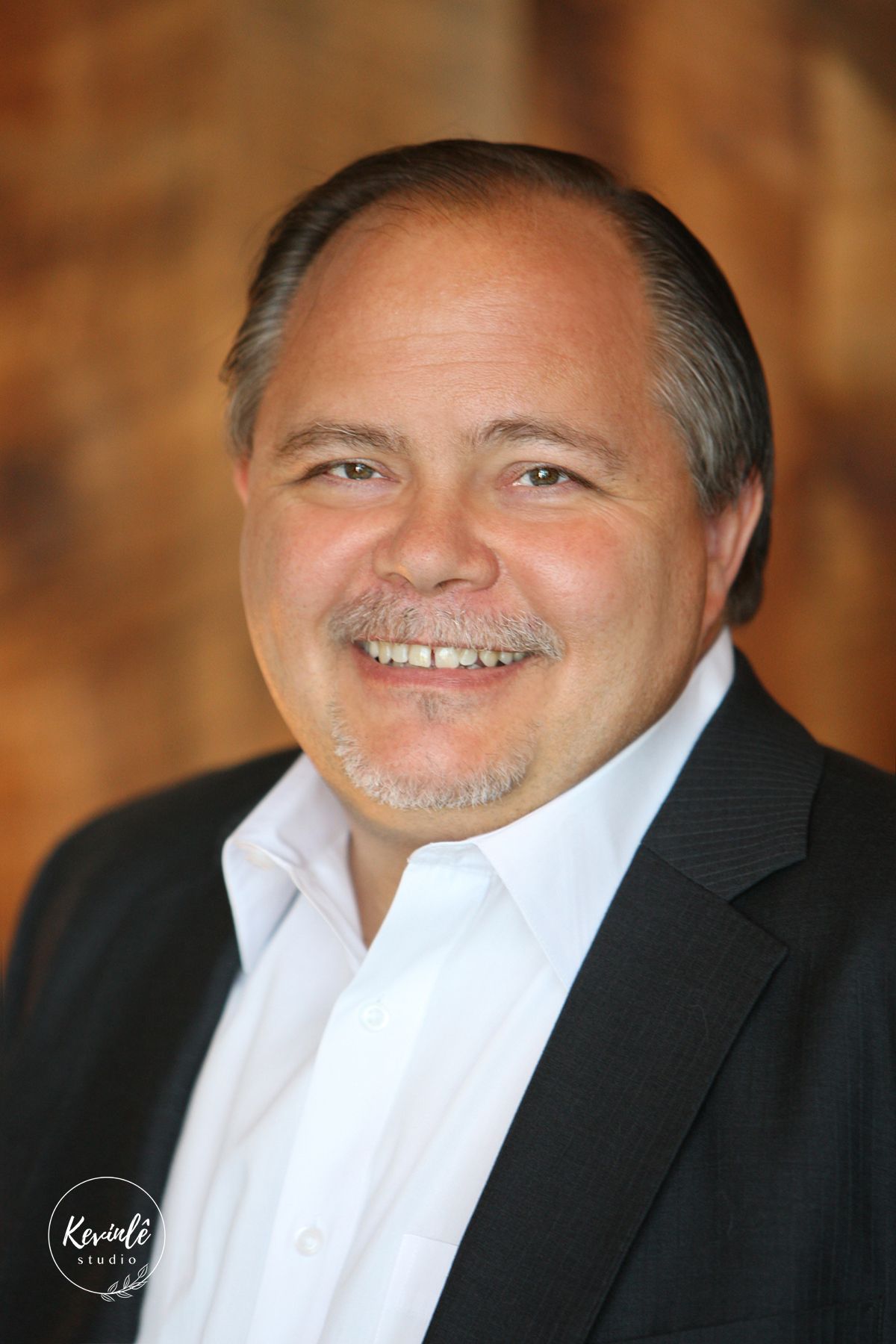 Professional portrait of a smiling man with gray hair wearing a dark suit jacket.