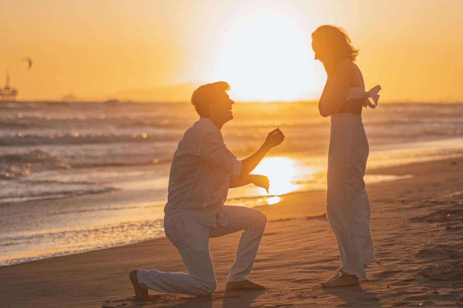 Beach proposal during golden hour with sun setting over ocean.