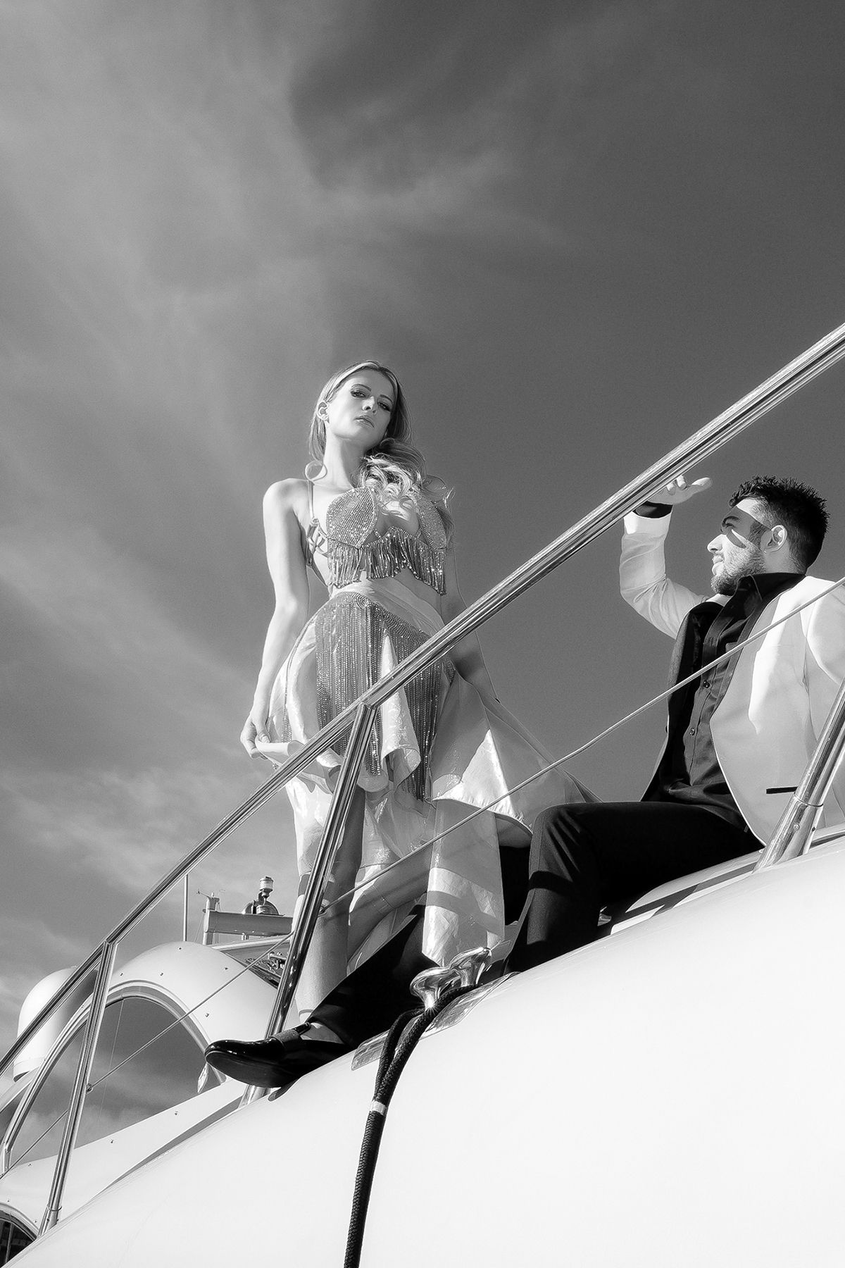 Low angle black and white artistic photograph showing figures against cloudy sky on elevated platform.