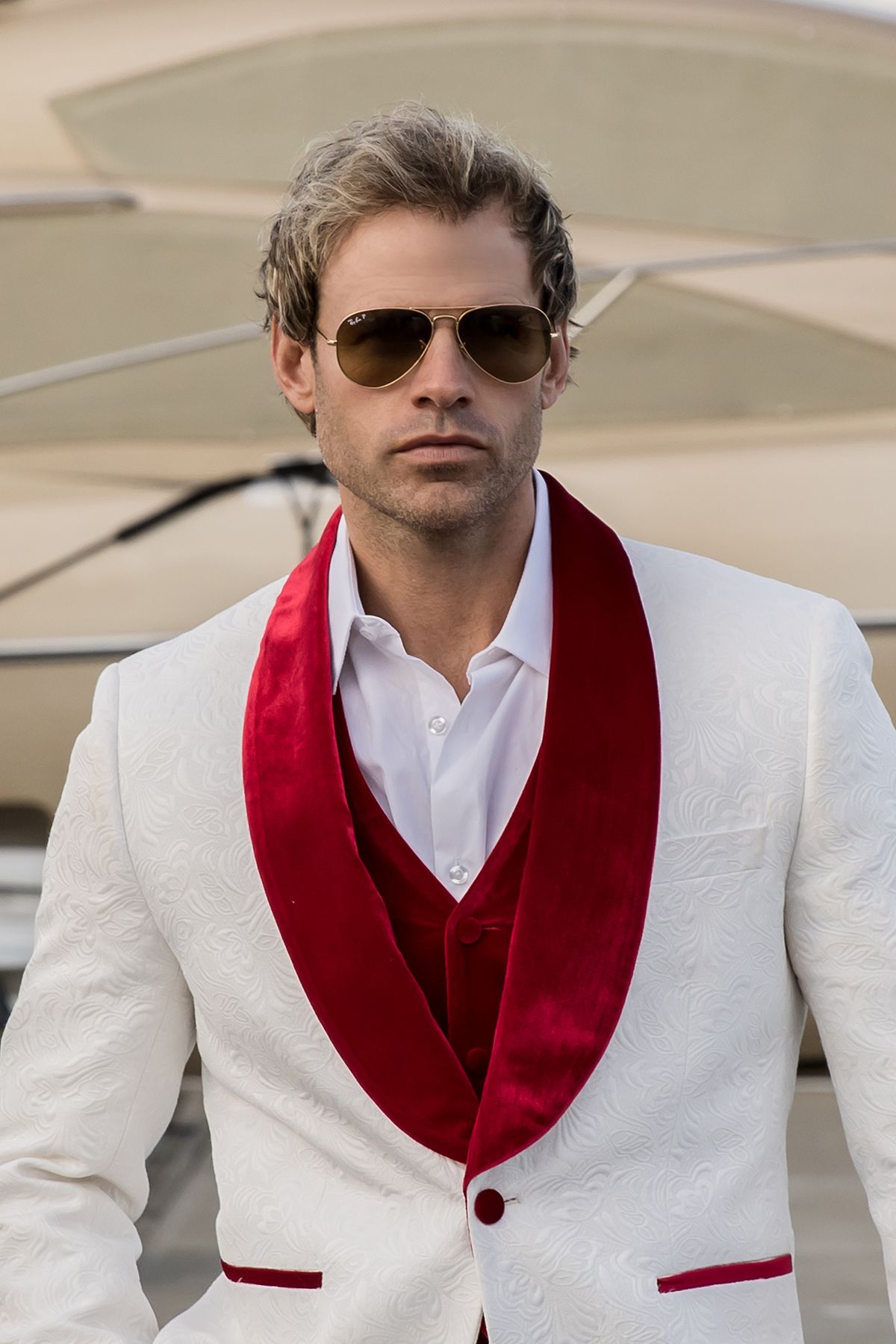 Fashion portrait in white suit with red shawl collar and aviator sunglasses.
