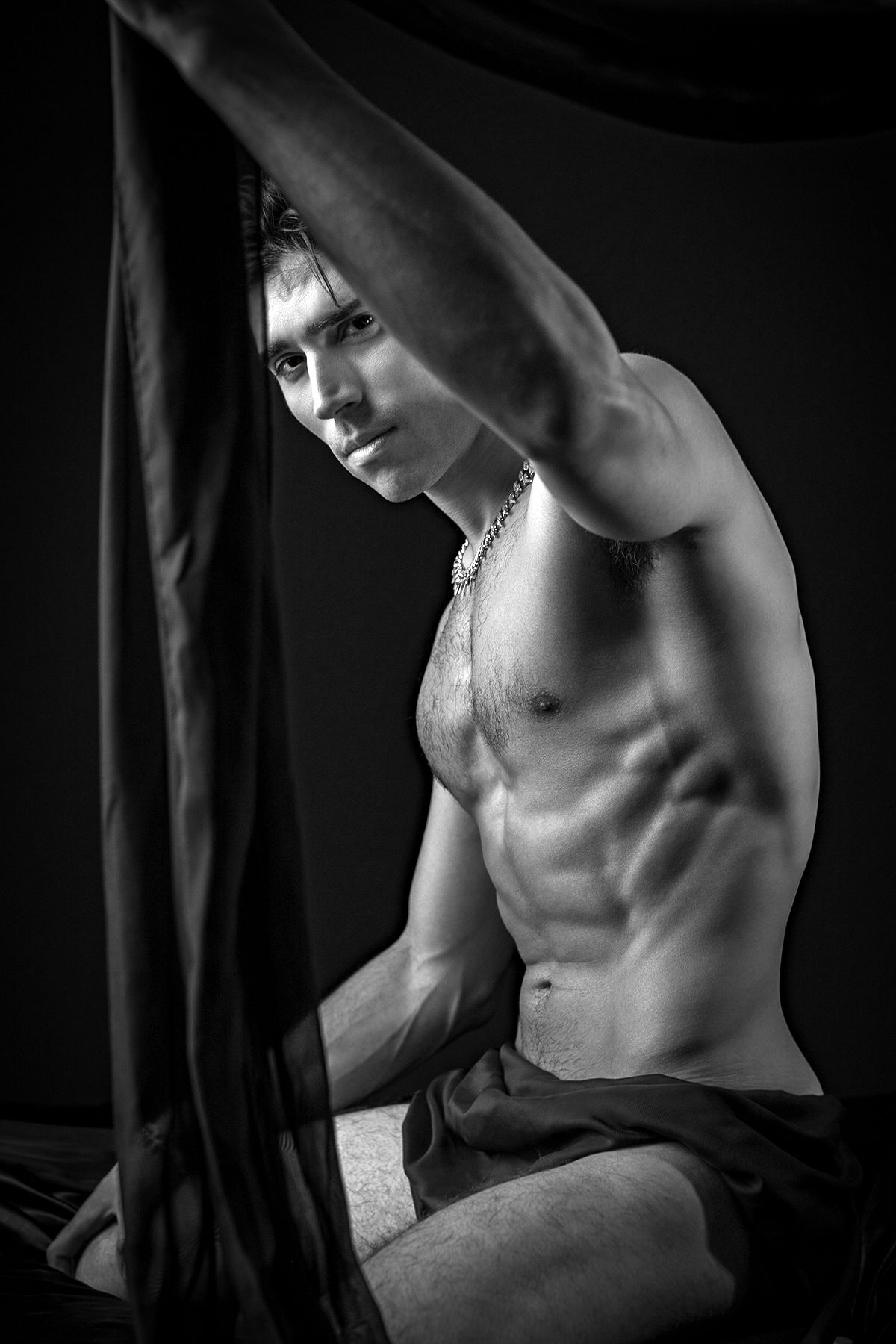 Artistic black and white photo showing muscular male physique in dramatic lighting against dark background.