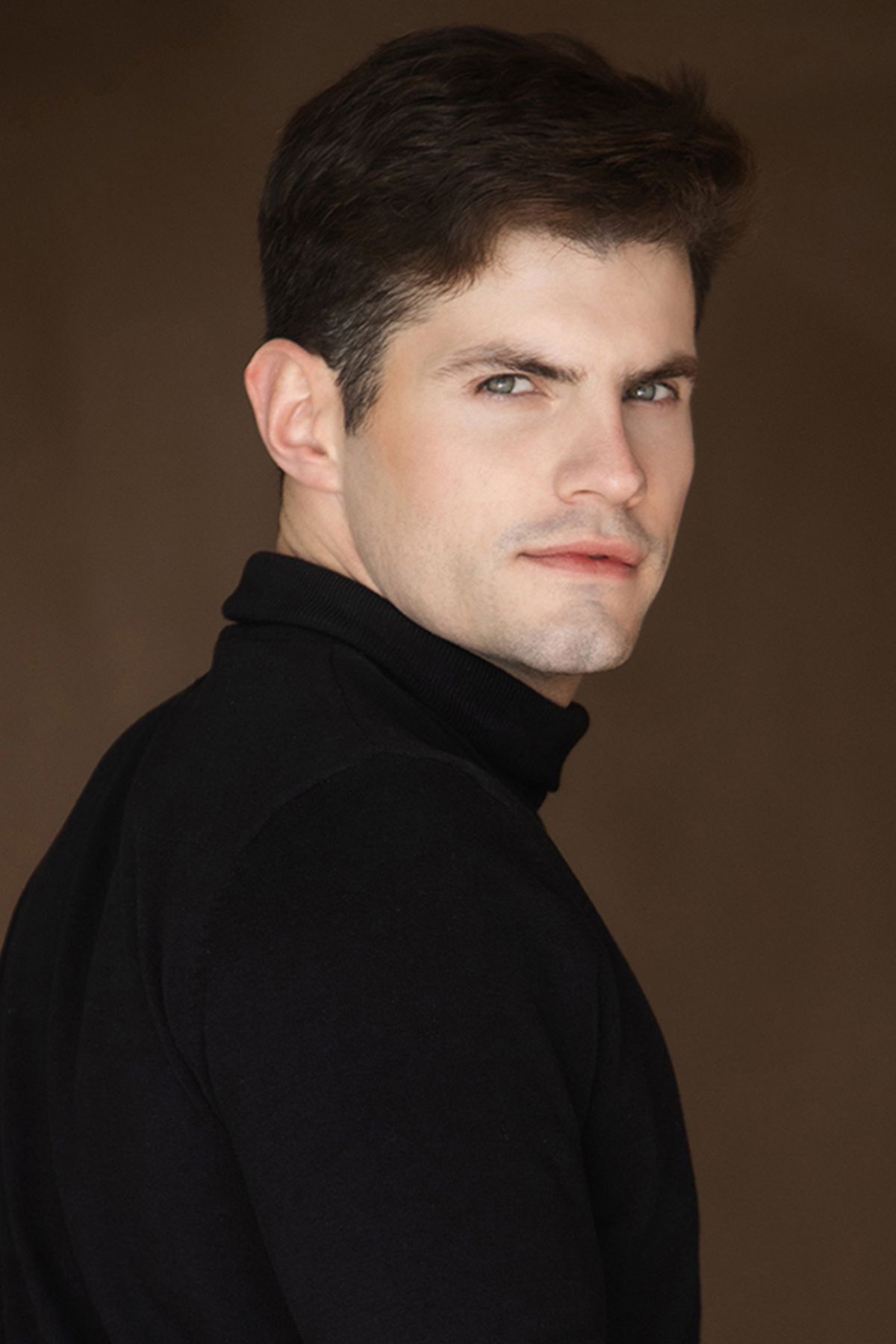 Model in black turtleneck against brown background.